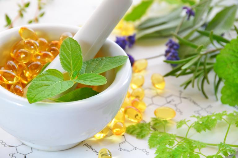 Soft gel supplements in a mortar surrounded by herbs